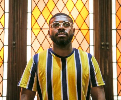 A young man staring ahead while standing in front of yellow stained glass