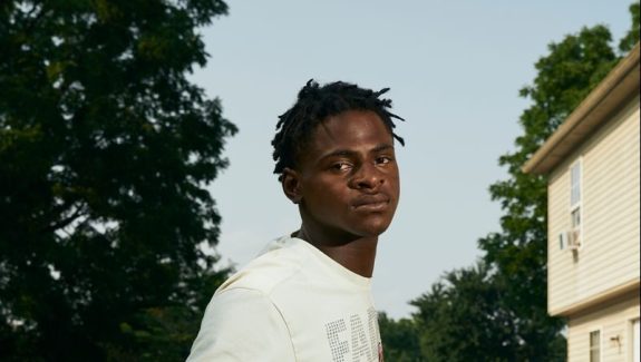 A young man leaning outside on a wooden fence