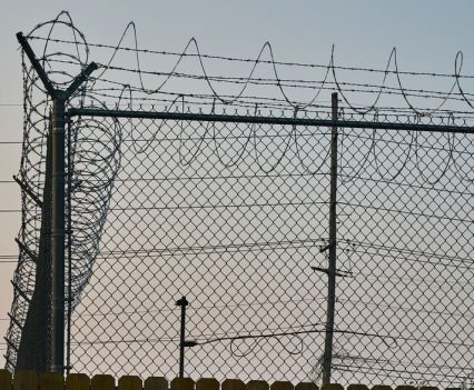 A tall barbed wire fence behind a wooden fence