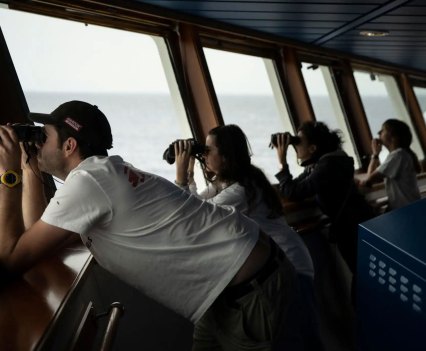 Rescue vessel crew use binoculars as they survey the ocean for migrants
