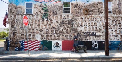 A mural on the side of a building with vintage photos of soldier's faces and large Mexican and US flags