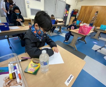 A closeup of a young student wearing a mask and working at a desk