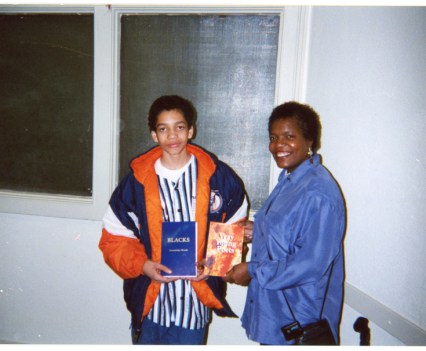 An older woman giving a book to a teen boy