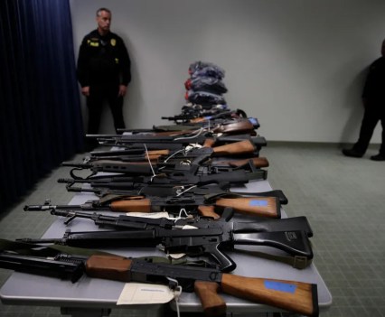 Two police officers stand near illegally possessed firearms displayed during a 2018 news conference about stepped up state and local enforcement of the Armed and Prohibited Persons System