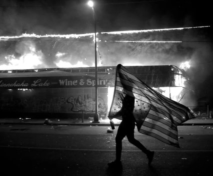 A protester carries an American flag upside down next to a burning building in Minneapolis last year