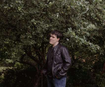 A man in all black standing among trees