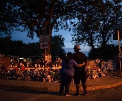 A hugging couple standing in front of an Uvalde Elementary School shooting tribute