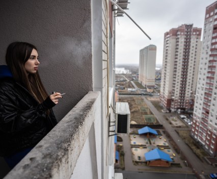Kateryna, 26, smokes at her balcony in Kyiv, Ukraine, on March 3, 2022. Most of her neighbors left the area, and the buzzing neighborhood is empty and quiet now. "It's hard to believe I could go for a run in the middle of the night with no concerns about my safety", Kateryna says.