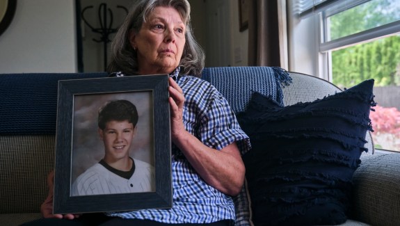 A woman sitting on a couch holding a framed photo of a young man