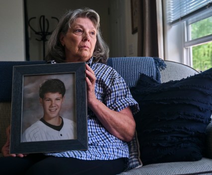 A woman sitting on a couch holding a framed photo of a young man