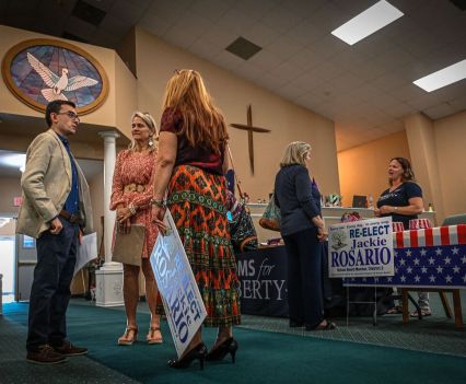 A woman holding a sign stands in a church holding a sign while talking to a man and a woman