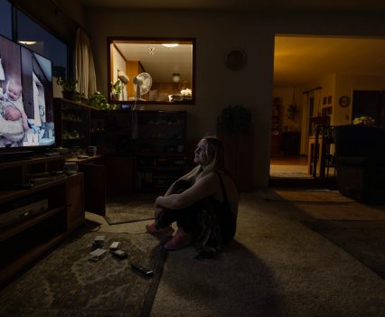 LOS ANGELES, CA - DECEMBER 18, 2022: Inside her Grandmothers Culver City living room December 18, 2022, Sarah Fay (pictured on the screen with her Grandpa, Matt, who passed away in a nursing home recently) watches a Christmas home movie from late 1990’s. Sarah’s Grandmother, Pat Fowler, filmed all the home movies and said “there’s nothing like a Grandchild … they’re just the best.” Sarah’s Mom is currently in hospital with Covid. Sarah’s housing problem is that she can’t find a place she can afford with a landlord that will take her even though she has a full-time job. She earns nearly $4K per month, but after years living between her car, at hotels, her mother’s place, and Grandmothers garage she doesn’t seem to be the ideal tenant to landlords and lives a life of housing insecurity at 28 years old. (Photo by Barbara Davidson)