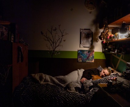 LOS ANGELES, CA - DECEMBER 18, 2022: Inside her Grandmothers cold Culver City garage, Sarah Fay, 28, settles into bed with her pet dogs. She is alone tonight because her Mother, who has lived in the garage for 13 years, is in hospital with Covid. Sarah is grieving the death of her “Grandpa” and worried about her Mother who is in hospital with Covid. Sarah’s housing problem is that she can’t find a place she can afford with a landlord that will take her even though she has a full-time job. She earns nearly $4K per month, but after years living between her car, at hotels, her mother’s place, and Grandmothers garage she doesn’t seem to be the ideal tenant to landlords and lives a life of housing insecurity at 28 years old. (Photo by Barbara Davidson)