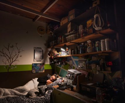 LOS ANGELES, CA - DECEMBER 18, 2022: Inside her Grandmothers cold Culver City garage, Sarah Fay, 28, settles into bed with her pet dogs. She is alone tonight because her Mother, who has lived in the garage for 13 years, is in hospital with Covid. Sarah is grieving the death of her “Grandpa” and worried about her Mother who is in hospital with Covid. Sarah’s housing problem is that she can’t find a place she can afford with a landlord that will take her even though she has a full-time job. She earns nearly $4K per month, but after years living between her car, at hotels, her mother’s place, and Grandmothers garage she doesn’t seem to be the ideal tenant to landlords and lives a life of housing insecurity at 28 years old. (Photo by Barbara Davidson)