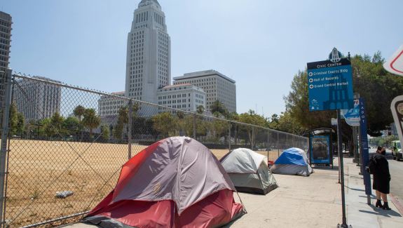 Three tents pitched on a sidewalk in front of a fence