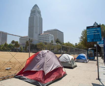 Three tents pitched on a sidewalk in front of a fence