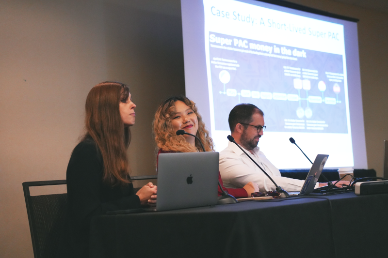 Three people sit in front of a presentation screen in a conference room. They are giving a presentation about open source intelligence.