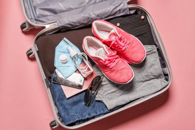 Open suitcase packed with shoes, mask, clothes and sunglasses