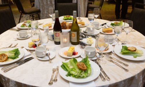 A table at the Online Journalism Awards Banquet at ONA22; plates with salad and bottles of wine are on the table.