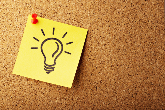 Yellow sticky note with lightbulb drawing is pinned to a cork message board.