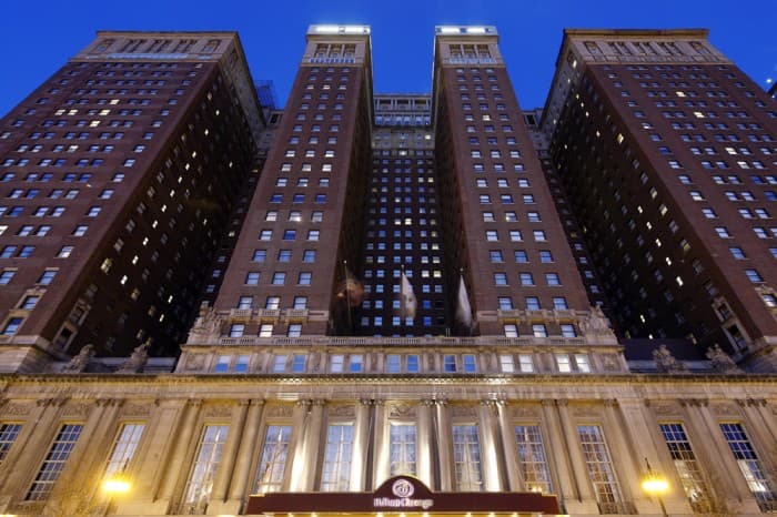 Exterior of the Hilton Chicago hotel at dusk, with illuminated entrance and tall brick towers.