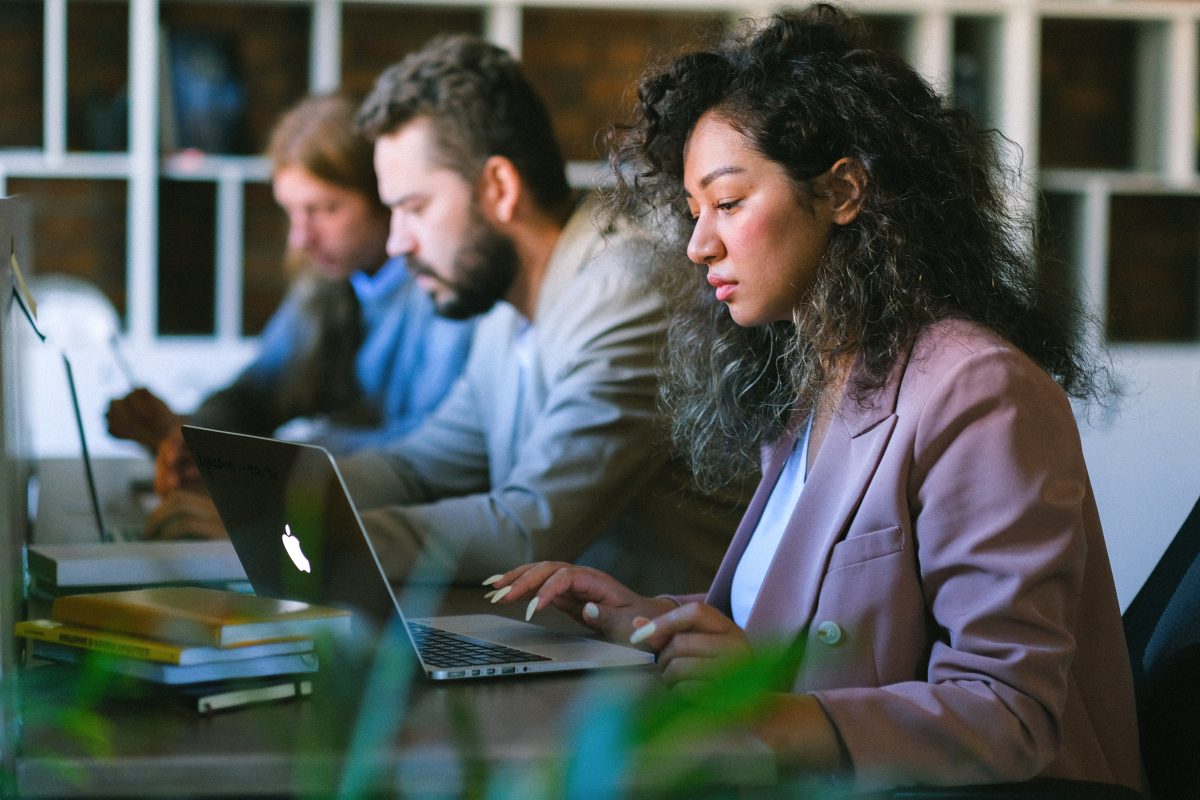 A stock image of several people seated at a table and looking at laptops.